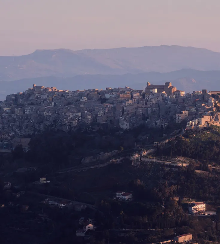 A hilltop village at dusk with mountains in the background